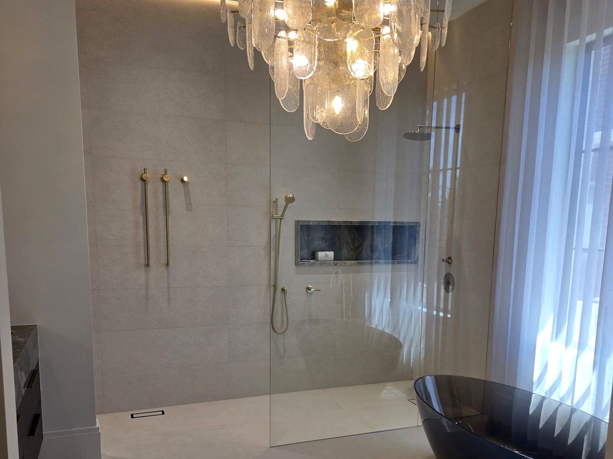 Luxury ensuite with a smoked-glass freestanding tub, crystal chandelier and a curbless walk-in shower with brushed-gold fixtures