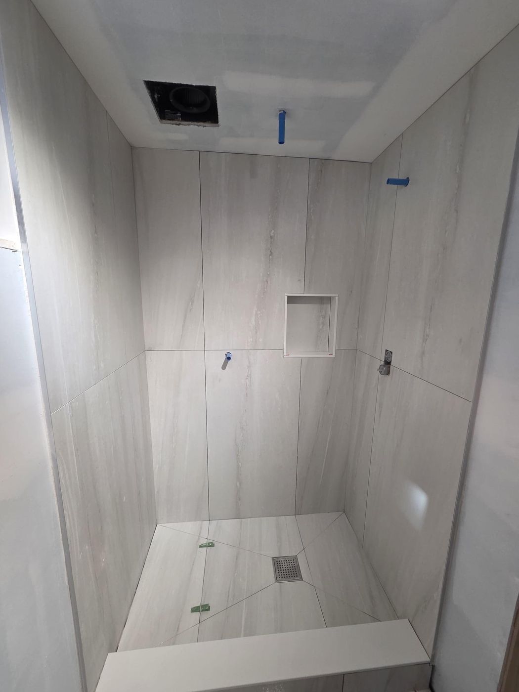 Large-format porcelain shower mid-renovation: floor sloped to a centre drain, recessed niche and valve rough-ins ready for fixtures